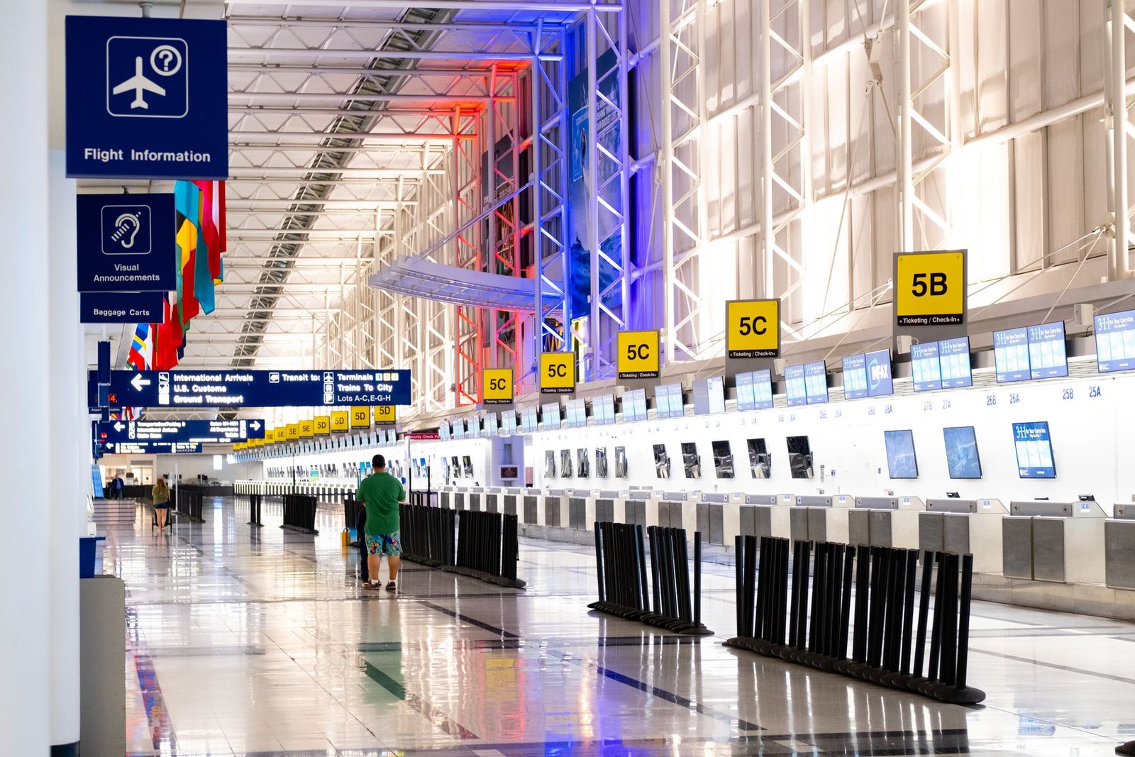 Bright modern airport departures hall with check-in counters, flight information screens and sunlight through a glass wall