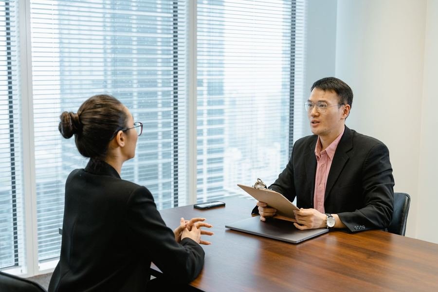 A travel consultant reviewing visa paperwork on a clipboard with a client across a desk in a bright office