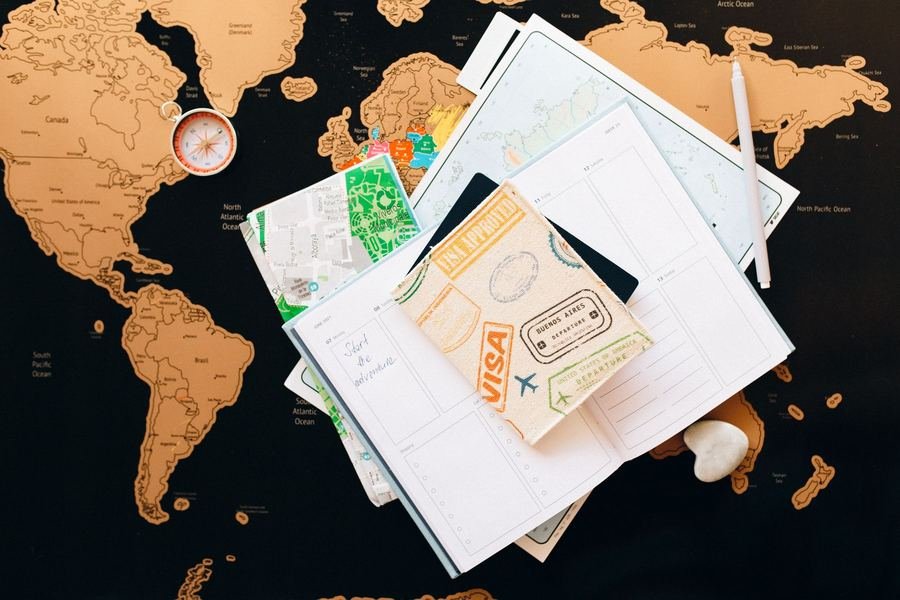Passport with entry stamps, a travel planner, folded maps and a compass laid out for a visa application